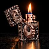 A decorative copper-toned lighter with an embossed snake design on the front and lid, shown open with a flame lit against a dark background. — view 3