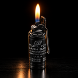 A black metal flashbang lighter with a visible flame, standing upright on a dark reflective surface against a black background — view 1